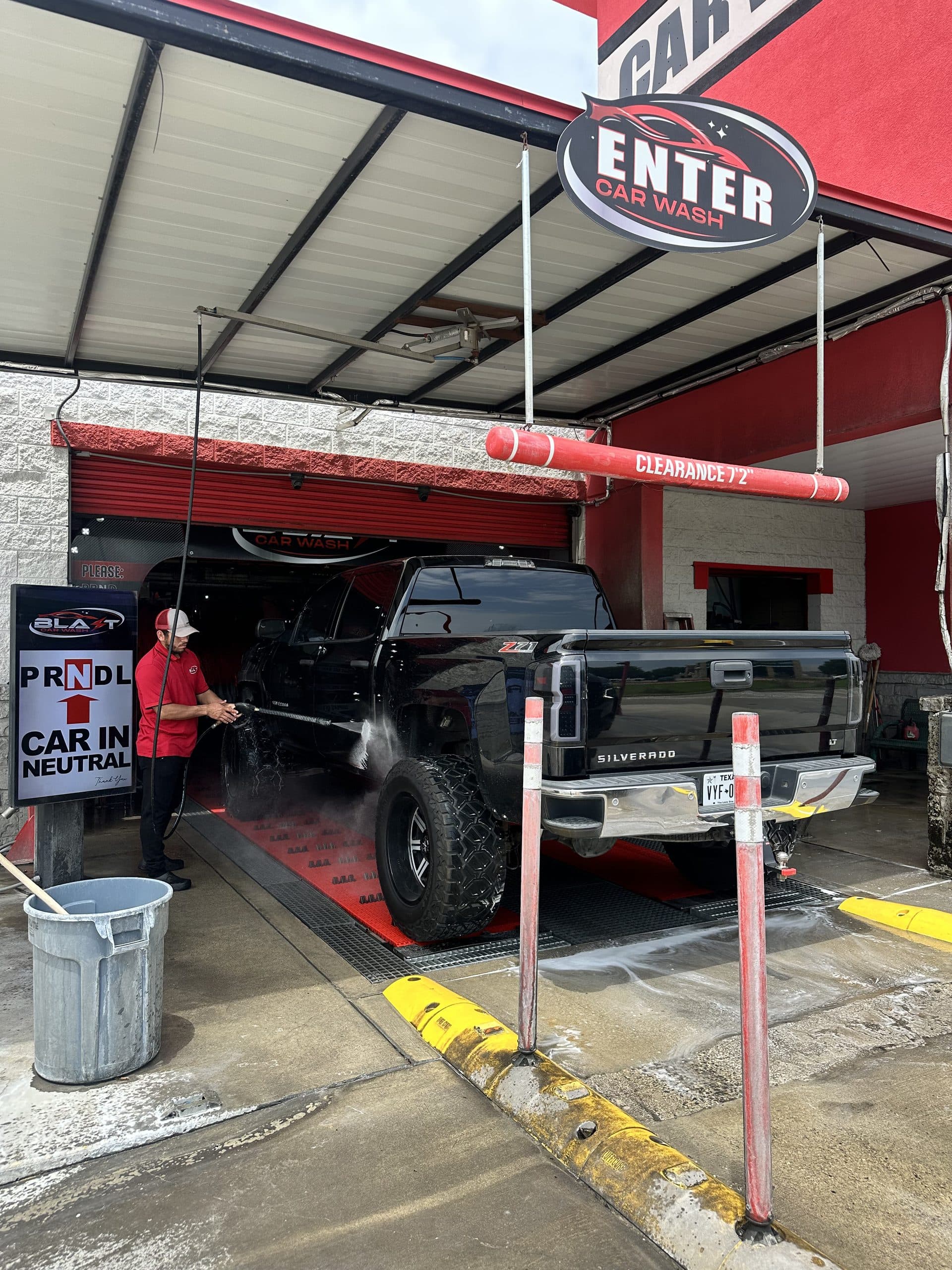Attendant pre-rinsing a pickup at the wash tunnel entrance